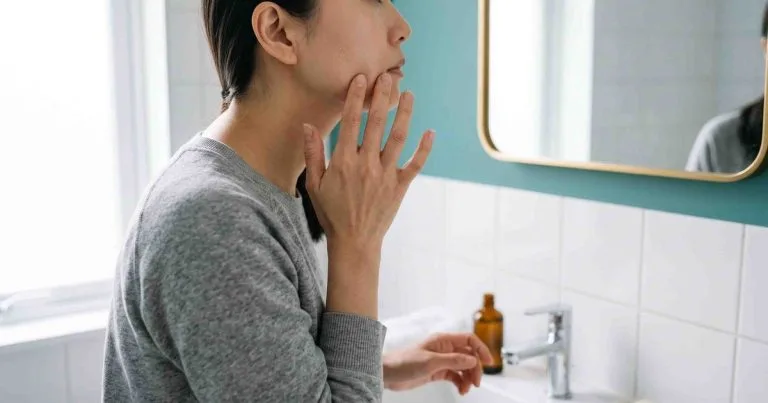 Mụn kê ở người lớn: các sẩn trắng nhỏ dưới bề mặt da vùng má soi trước gương phòng tắm